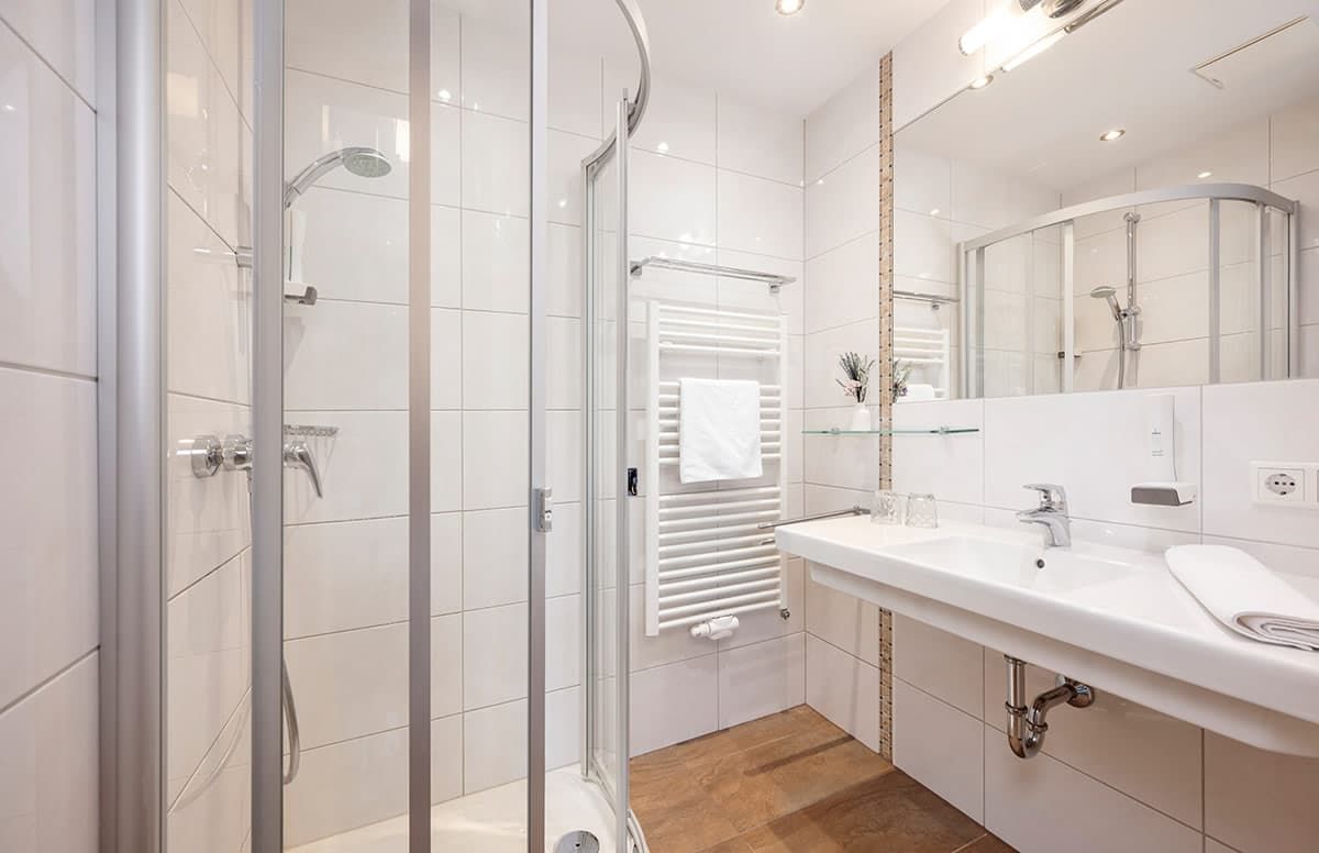 Een moderne badkamer met een glazen douchecabine, een witte wastafel en een grote spiegel.