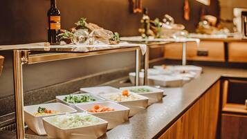 A buffet setup with various food containers and a bottle of wine.