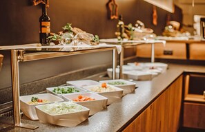A buffet setup with various food containers and a bottle of wine.