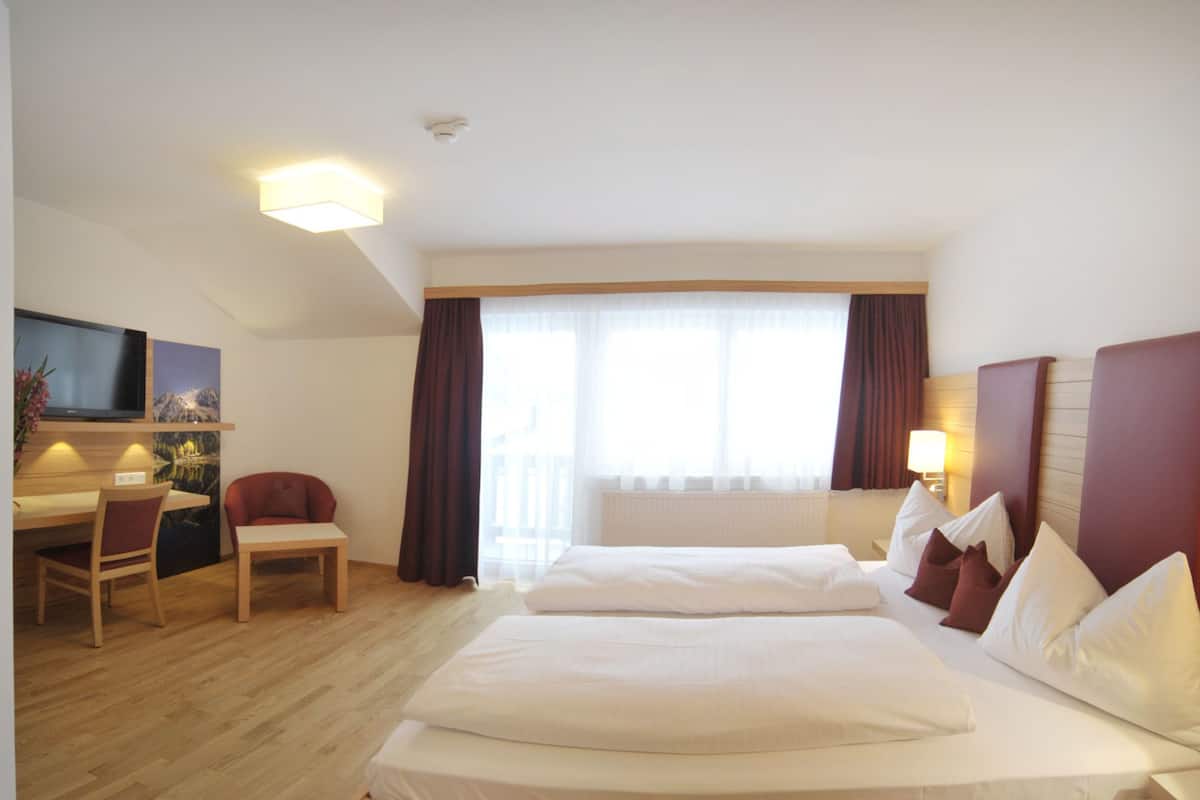 Une chambre d’hôtel avec un lit, un bureau, une chaise, une télévision et une fenêtre avec des rideaux.