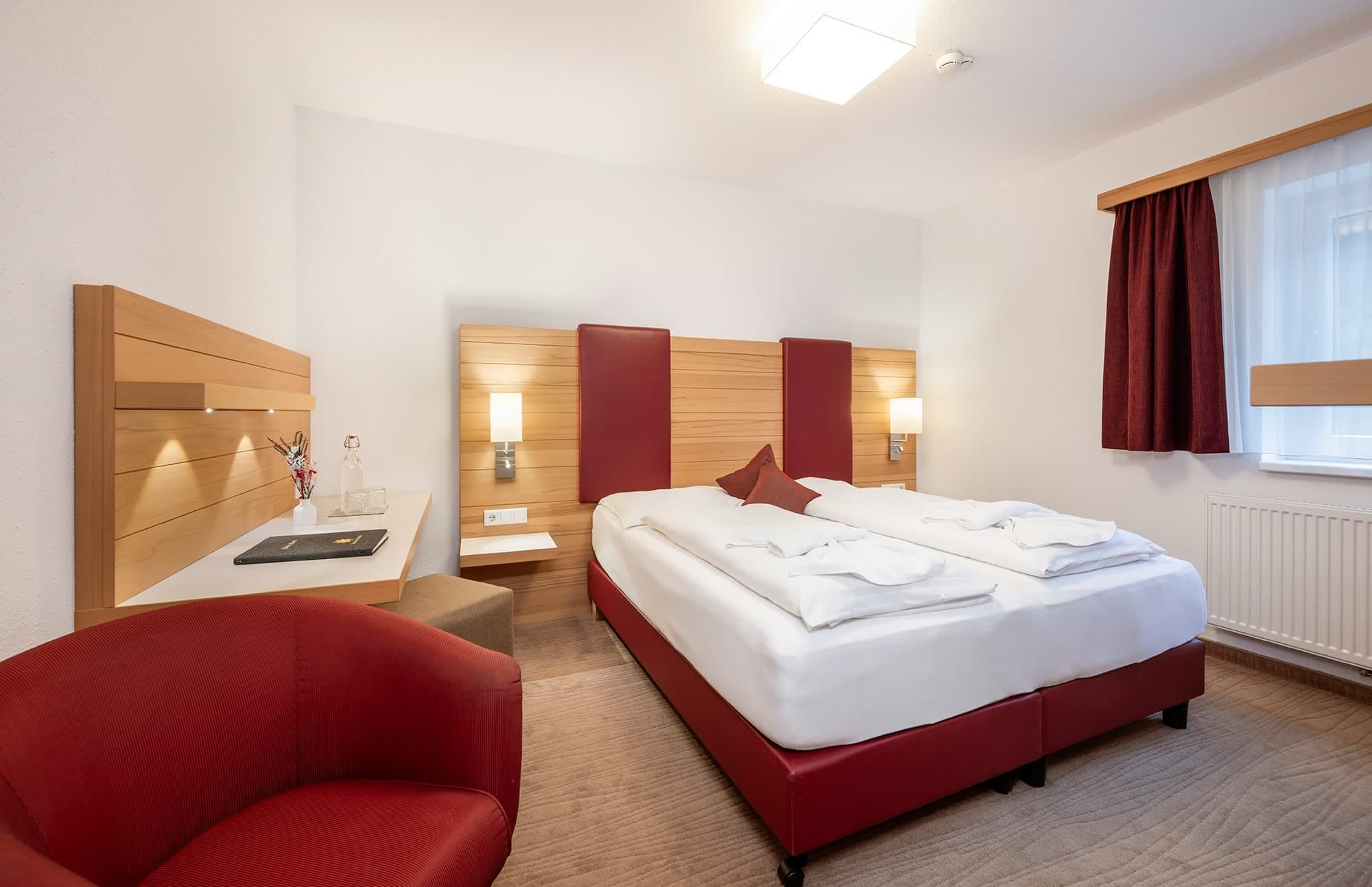 Ett hotellrum med en säng, ett skrivbord, en stol och ett fönster med gardiner.