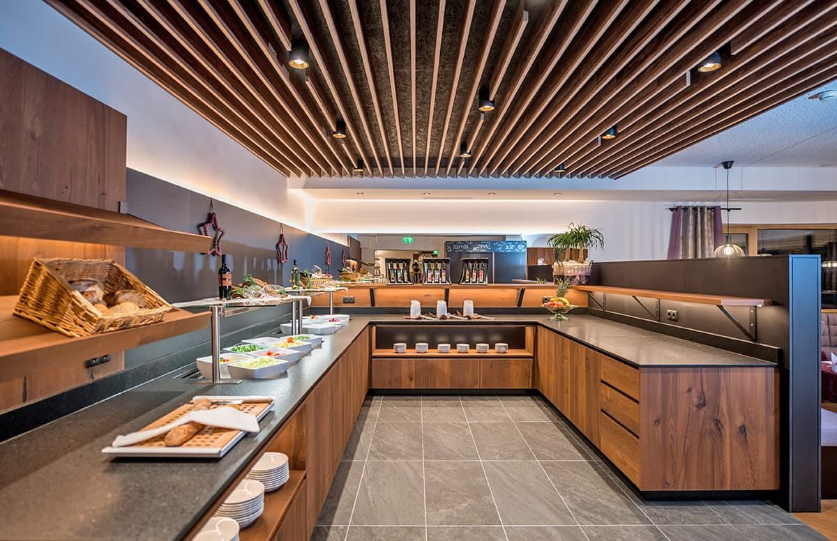 A modern breakfast bar with a wooden design, a variety of food items, and a seating area.