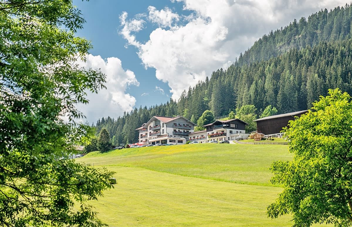 Un hotel con varias construcciones, un campo cubierto de césped y una montaña boscosa al fondo.