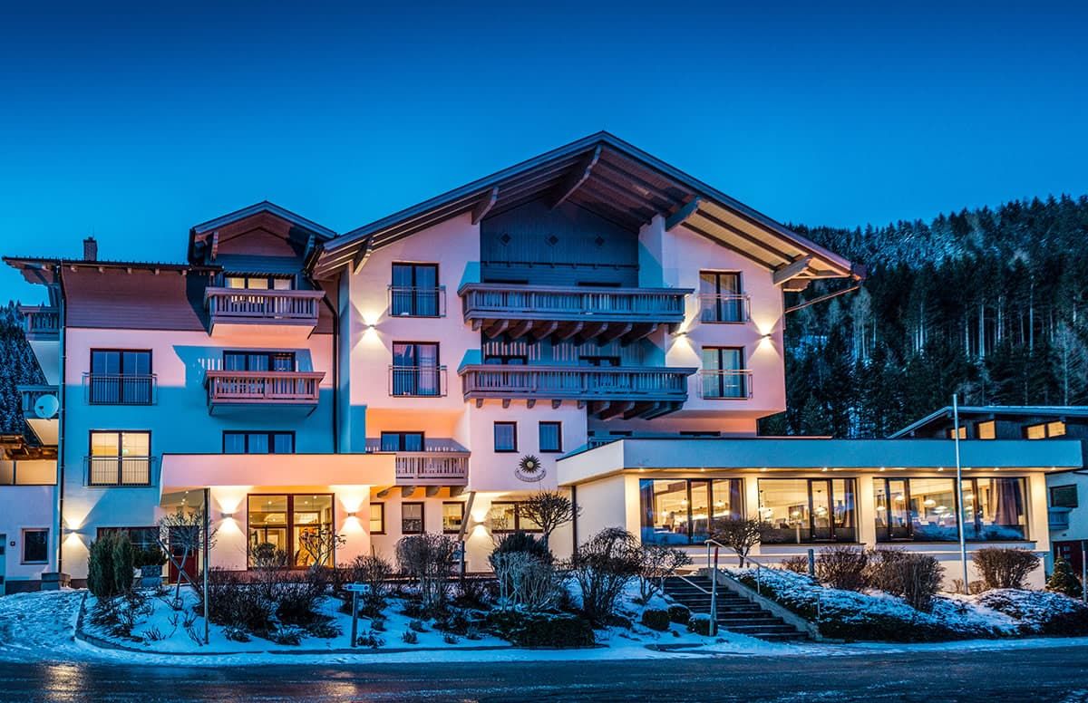 Ein mehrstöckiges Hotel mit Balkonen, im Hintergrund ein Skiabhang und ein gut beleuchteter Eingang.