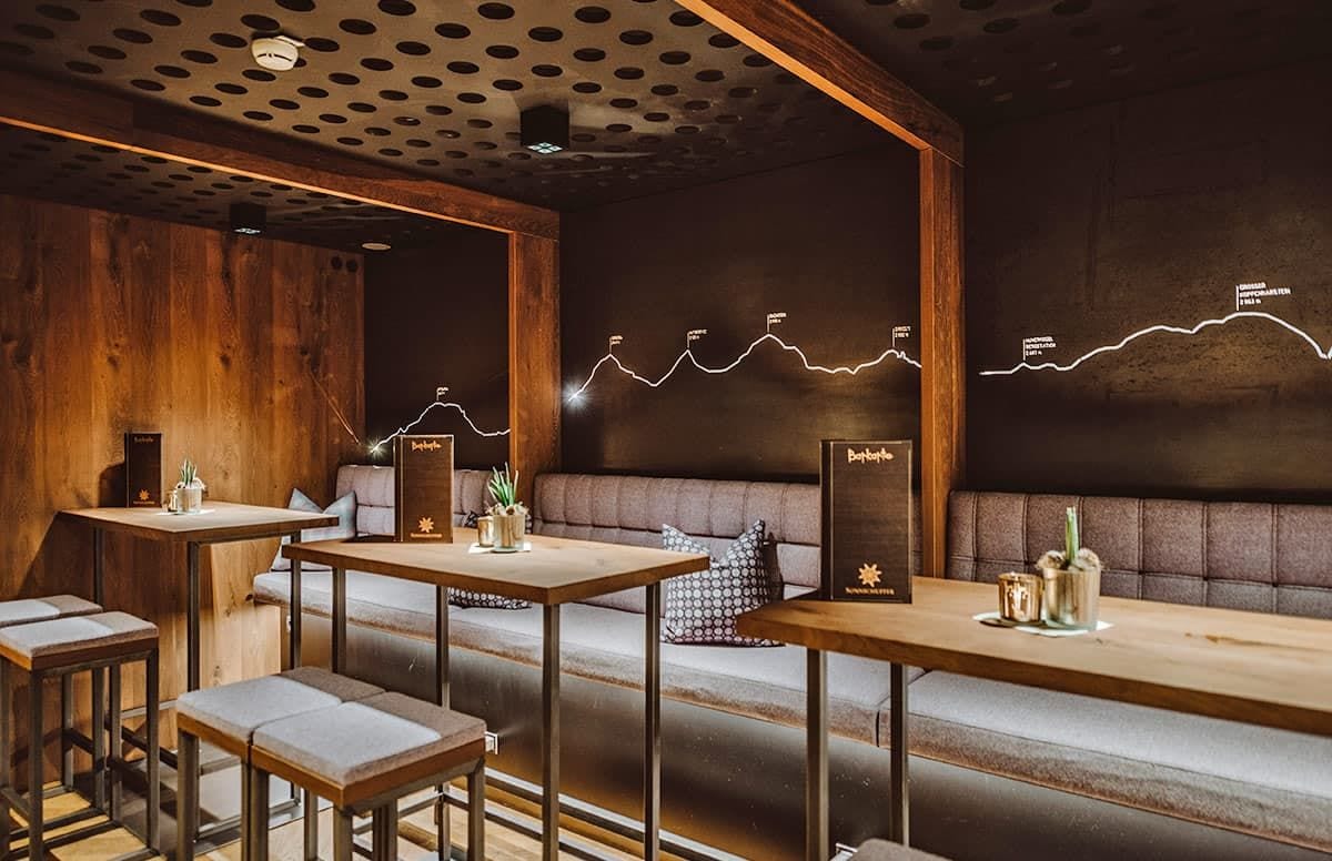 Interno di un ristorante con tavoli e panche di legno, un muro con un grafico a linee e un soffitto con motivi circolari.