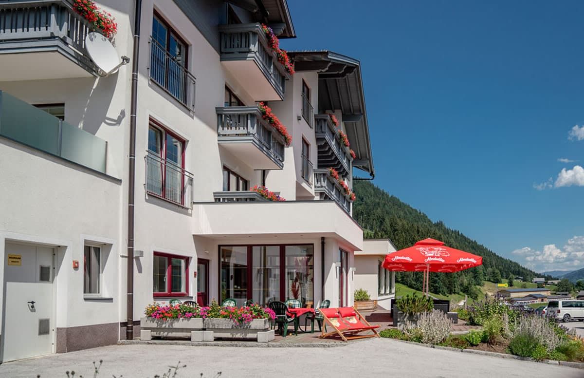 A multi-story hotel with balconies adorned with flowers, a covered outdoor seating area, and a view of the surrounding landscape.