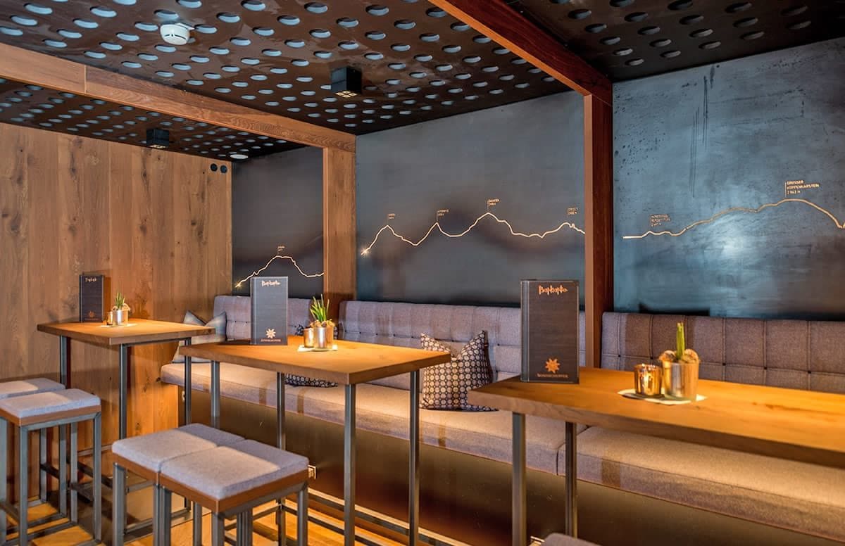 Un interior moderno con paneles de madera, un sofá, mesas y un original sistema de iluminación en la pared.