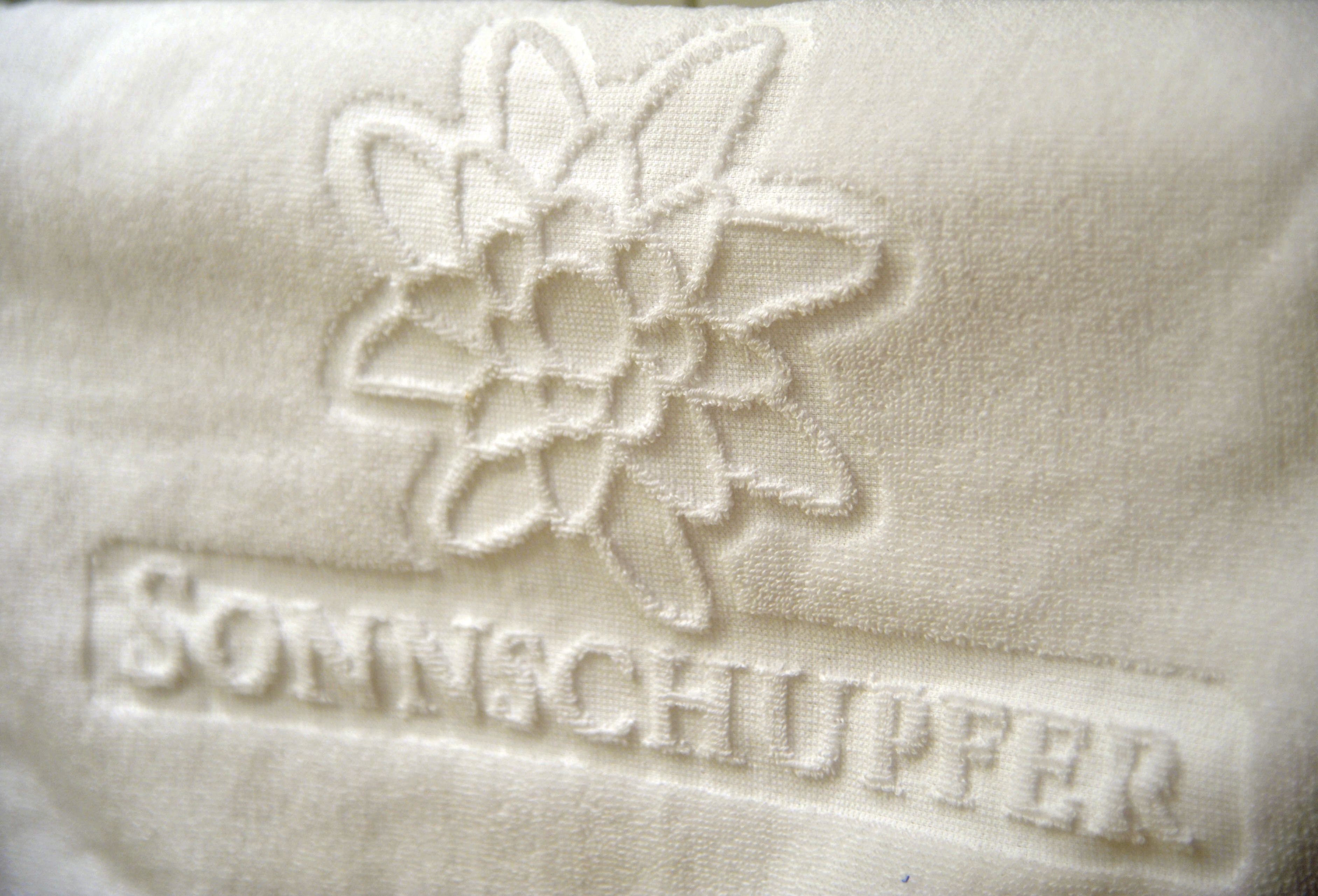 Primer plano de un tejido con una flor bordada y el texto "SONNENCHUPPER".