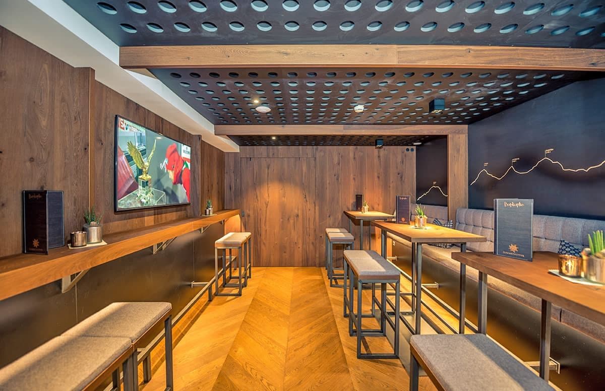 Un bar moderno con paredes de madera, una pantalla de televisión y una barra con taburetes.