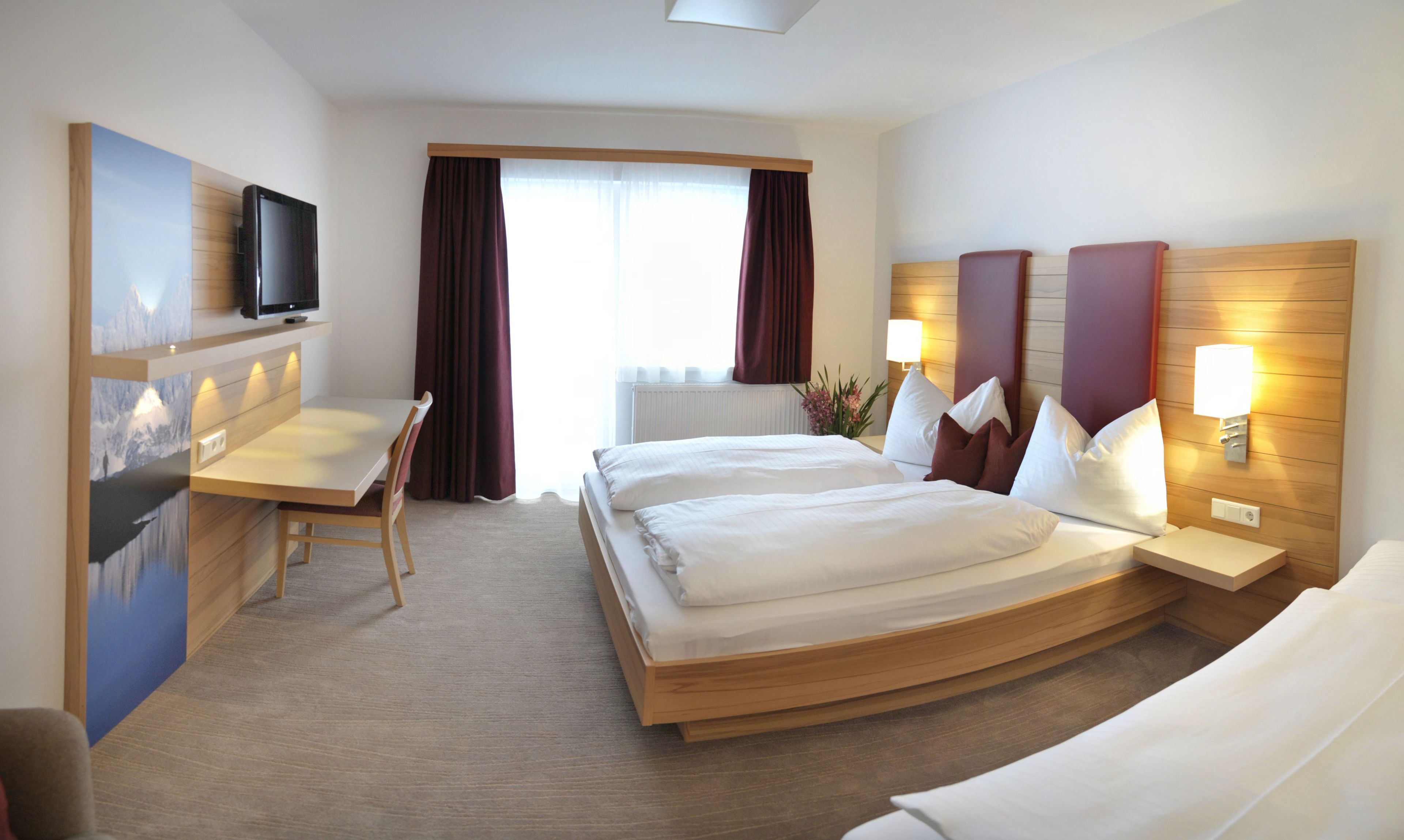 A hotel room with a bed, a desk, a chair, a television, and a window with curtains.