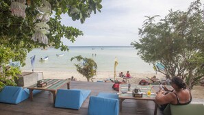 A beachside seating area with a view of the sea, a wooden table, and blue cushions. - Bubble Bungalow (Koh Tao)