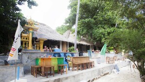 A beachside restaurant with outdoor seating, a thatched-roof structure, and a flag. - Bubble Bungalow (Koh Tao)