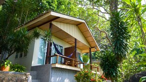 A two-story house with a balcony, surrounded by lush greenery and a stone wall. - Bubble Bungalow (Koh Tao)