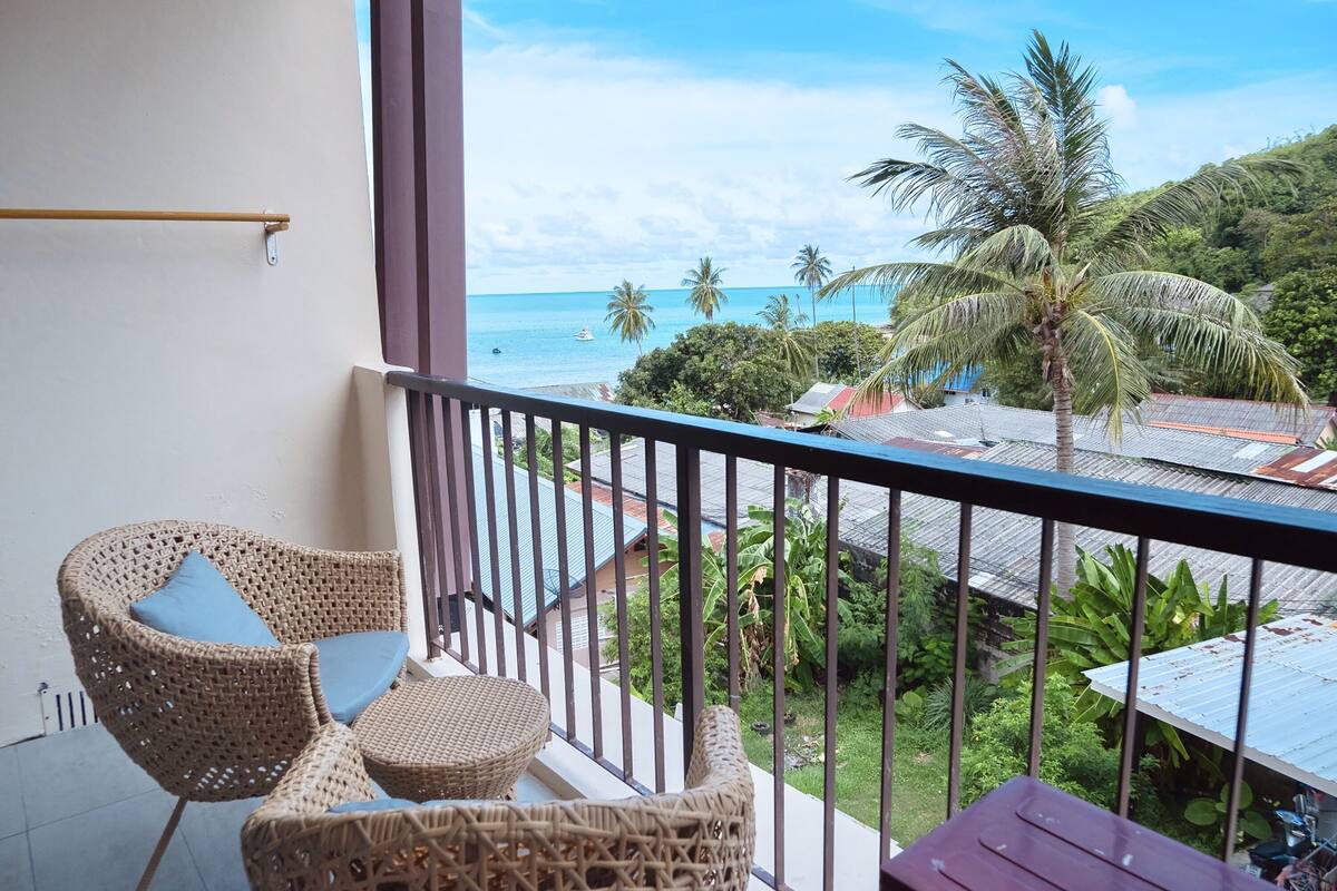 A balcony with wicker furniture and a view of the ocean and palm trees.