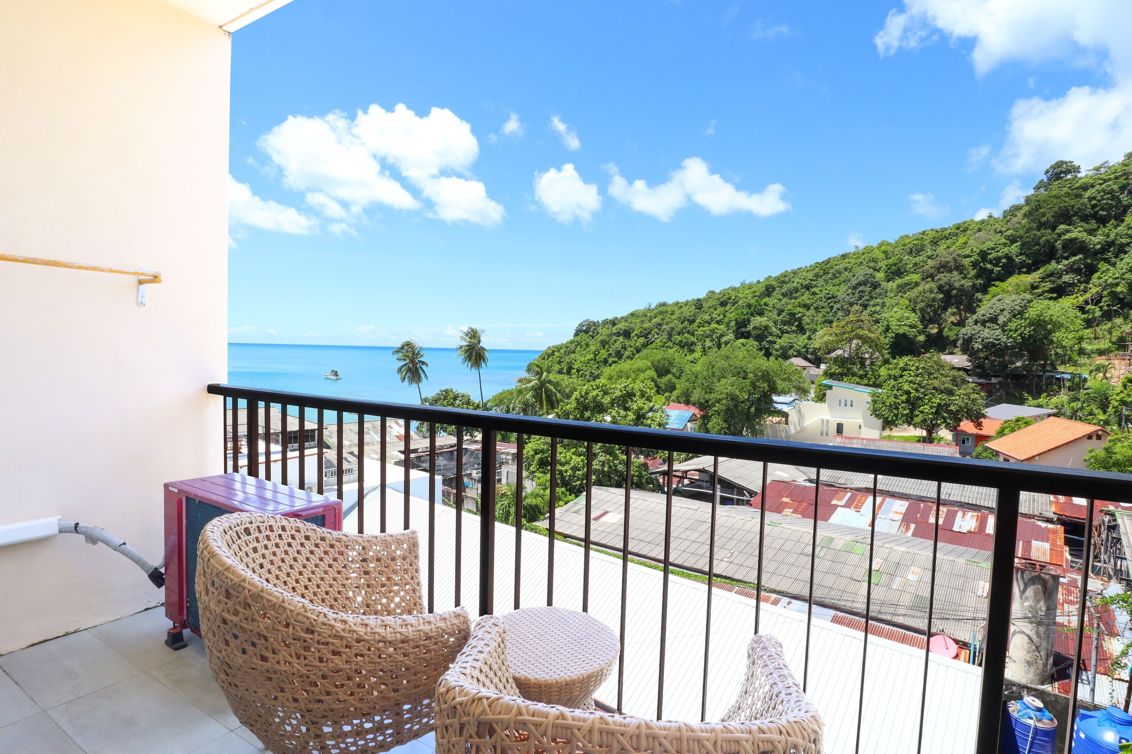 A balcony with wicker furniture, a view of the sea, and a green hillside.