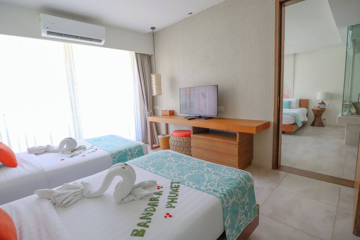 A hotel room with two beds, a desk, a television, and a large mirror.