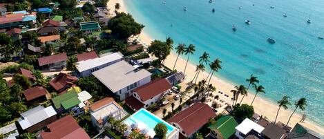 An aerial view of a coastal residential area with houses, a beach, and boats in the water.