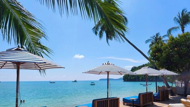 A wooden deck with lounge chairs and striped umbrellas overlooking a calm sea with boats. - Bandara Beach Resort, Phuket (Wichit)