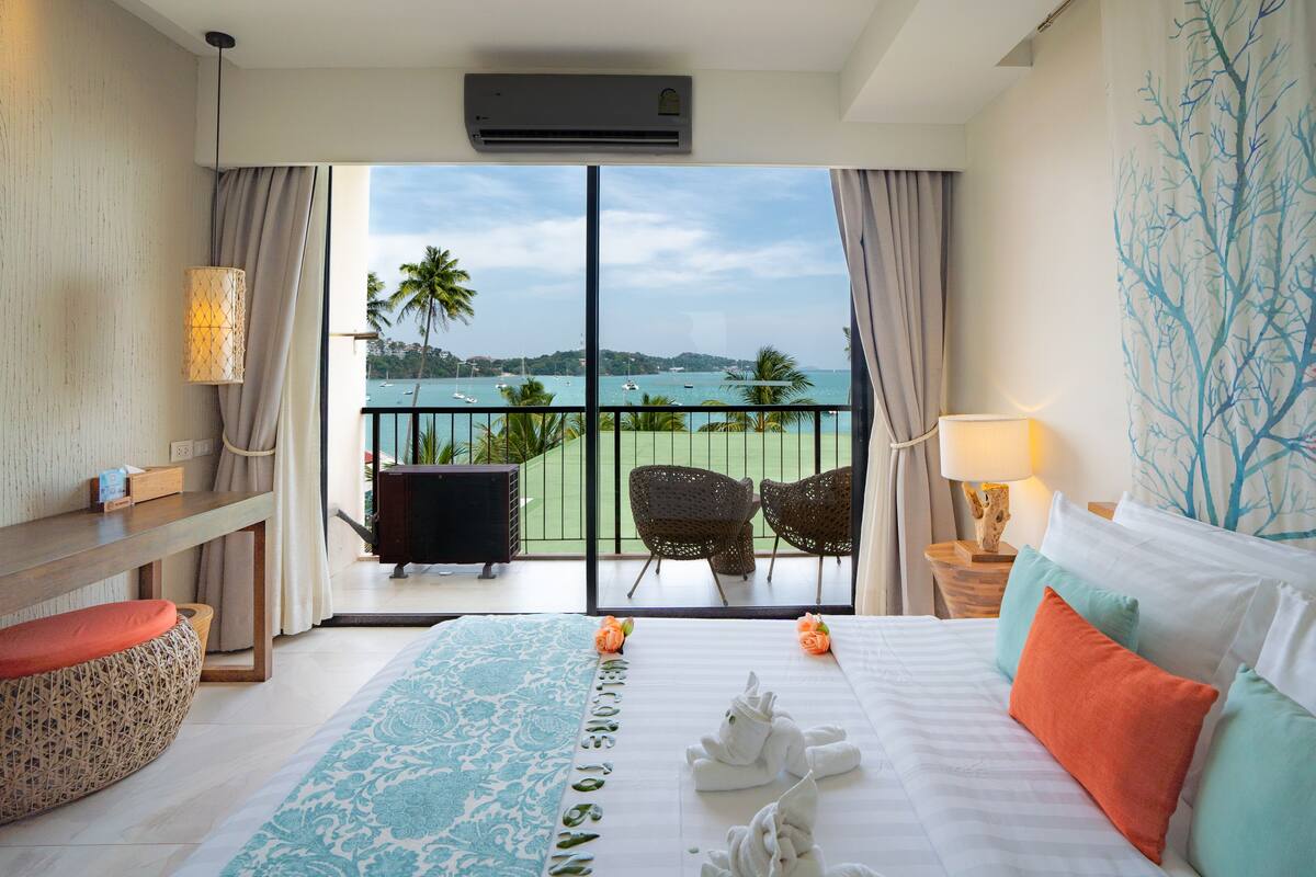 A hotel room with a large bed, a balcony with chairs, and a view of the sea.