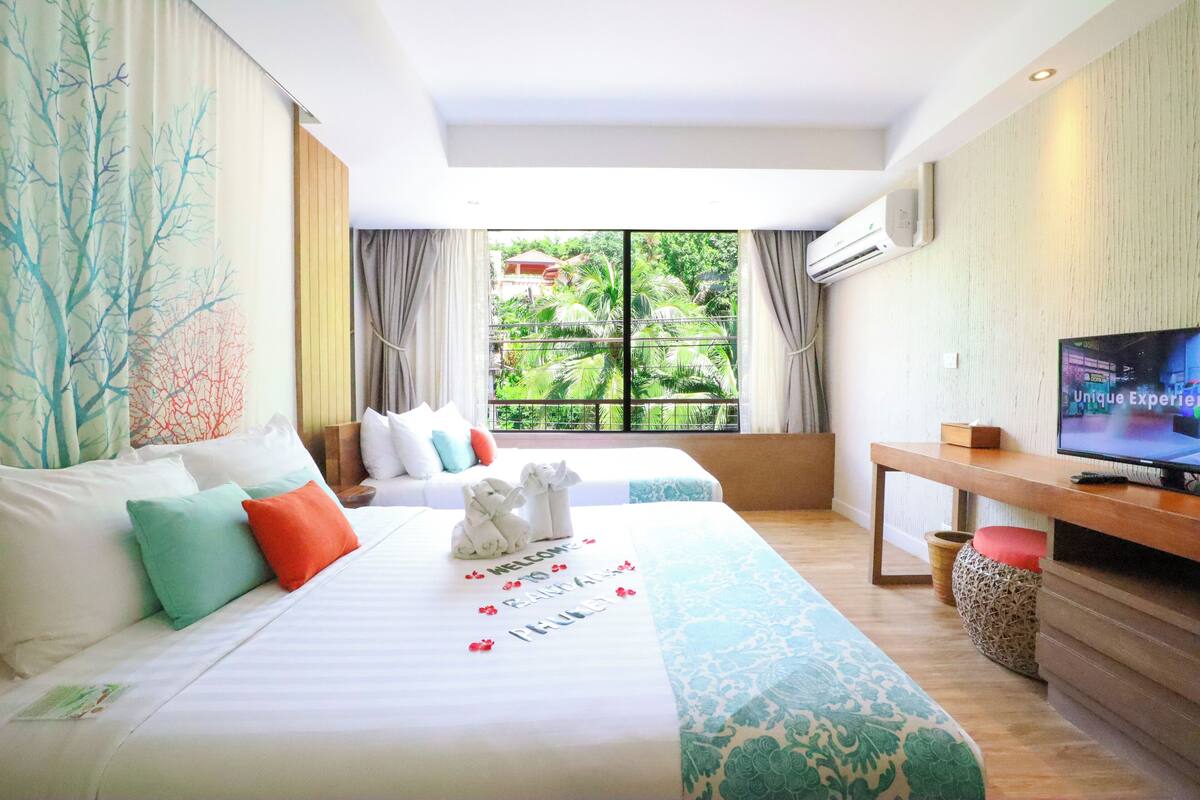 A hotel room with a large bed, a TV, and a window with a view of greenery.