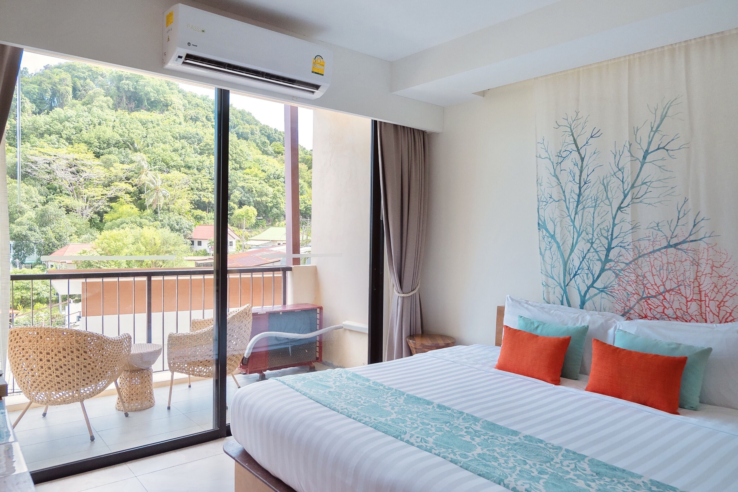 A hotel room with a balcony, a bed with multiple pillows, and a painting of trees on the wall.