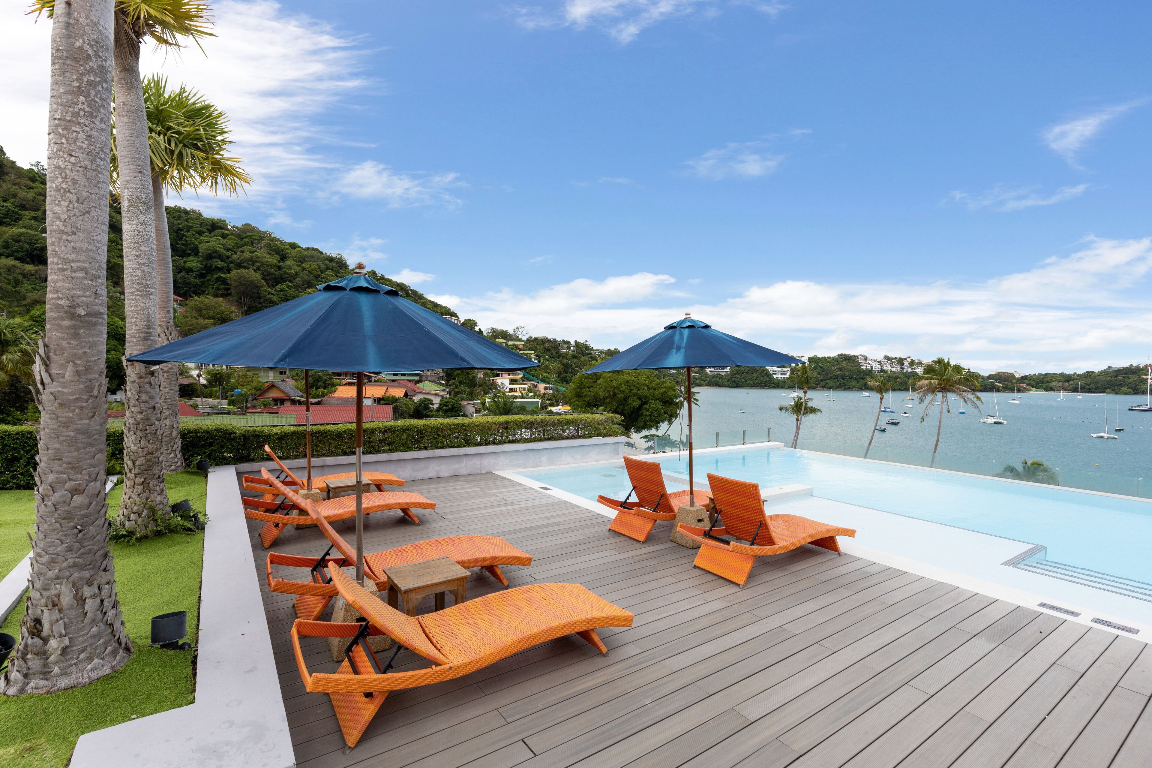 A poolside area with lounge chairs and umbrellas, overlooking a body of water with boats.