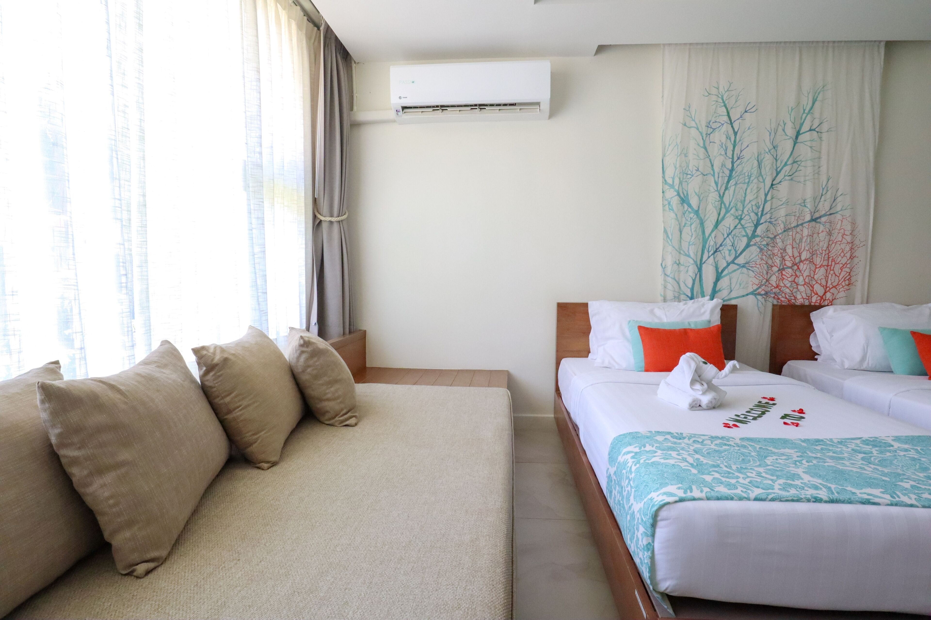 Una habitación de hotel con sofá, dos camas, aire acondicionado y una ventana con cortinas.
