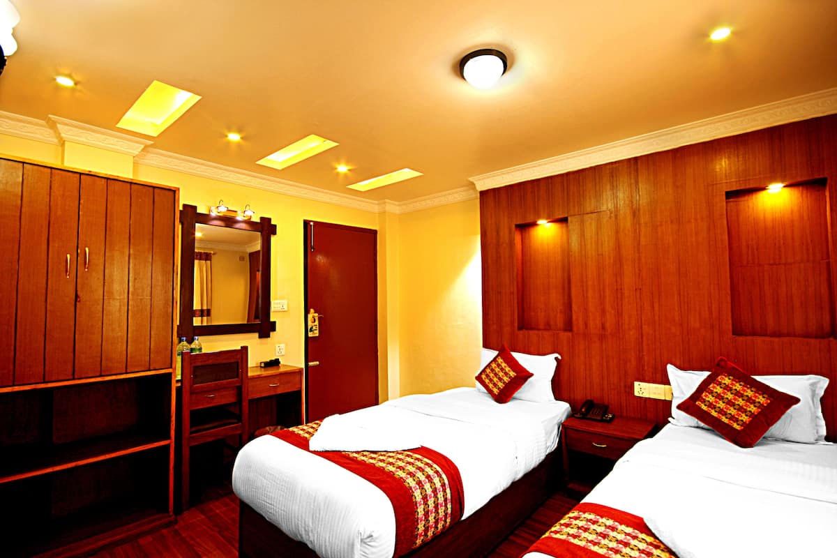 A hotel room with two beds, wooden wardrobe, a desk with a chair, and a mirror.