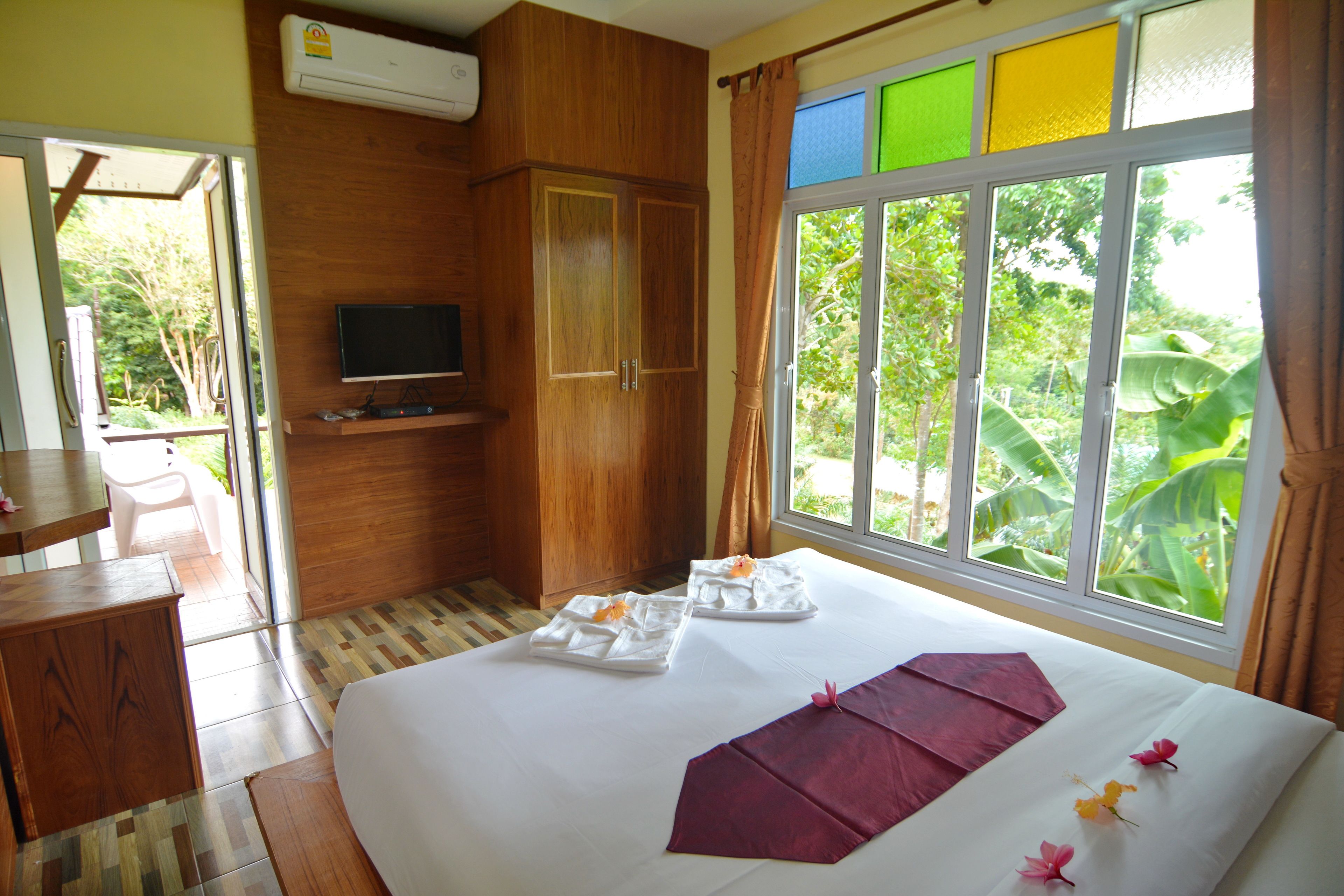 Ein Hotelzimmer mit Bett, Fernseher, Holzschrank und Fenster mit Blick auf Grünflächen.