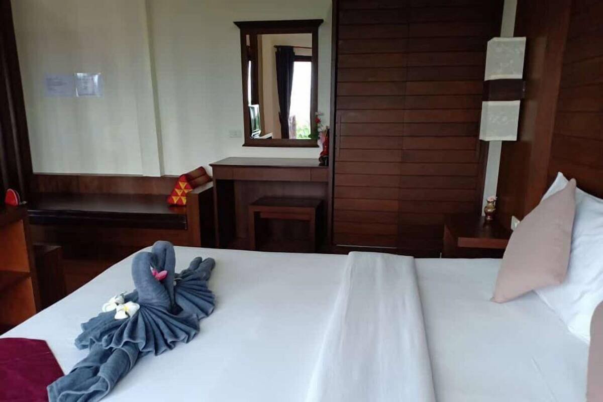A hotel room with a neatly made bed, a wooden desk, a mirror, and a small table.