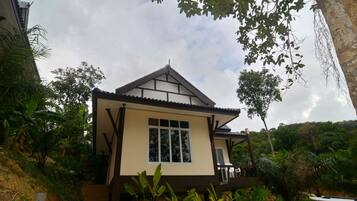 A two-story house with a balcony, surrounded by lush greenery and trees.