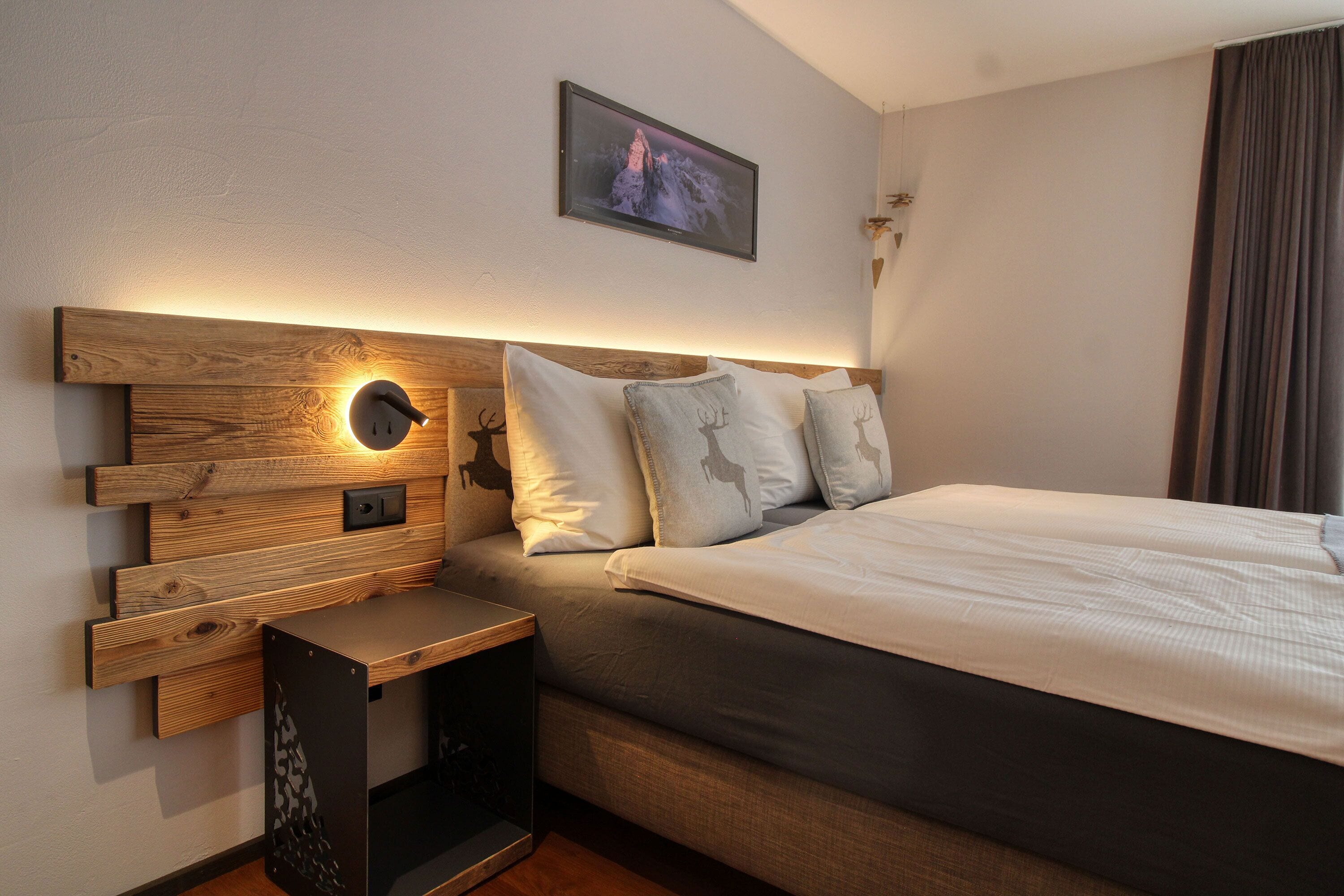 Une chambre d’hôtel moderne avec une tête de lit en bois, un téléviseur à écran plat fixé au-dessus du lit et une petite table de chevet avec une lampe.