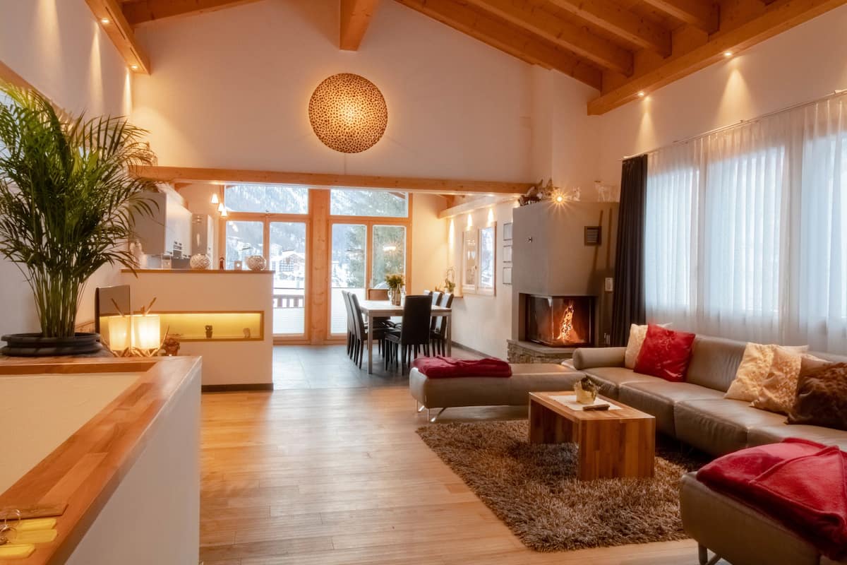 A spacious living area with a wooden ceiling, a fireplace, and a dining area visible through large windows.