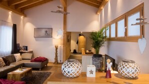 A spacious living room with a high ceiling, wooden beams, a sofa, a coffee table, decorative globes, and a potted plant. - Chalet A la Casa (Zermatt)