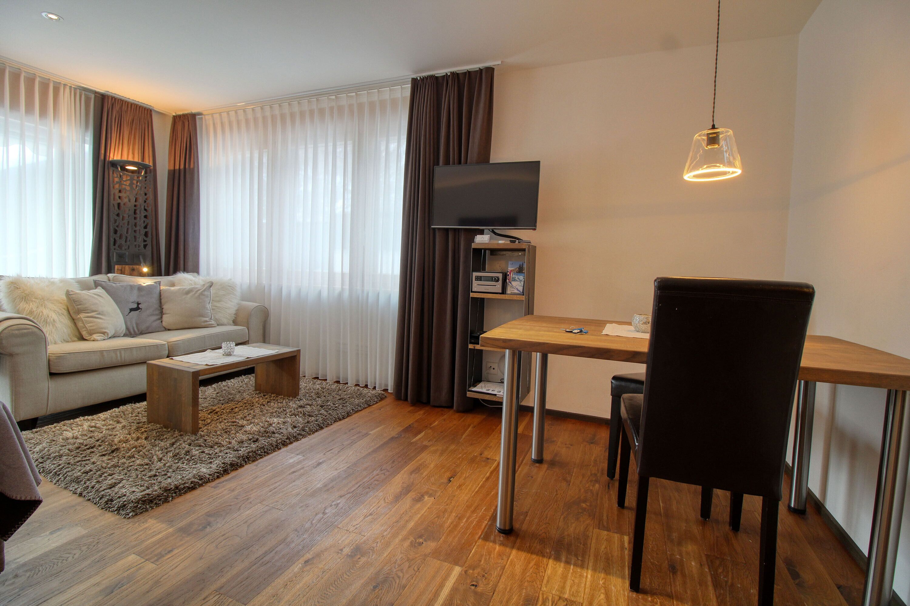 Un salon moderne comprenant un canapé, une table basse et un coin repas avec une table et des chaises. Un téléviseur à écran plat est fixé au mur.