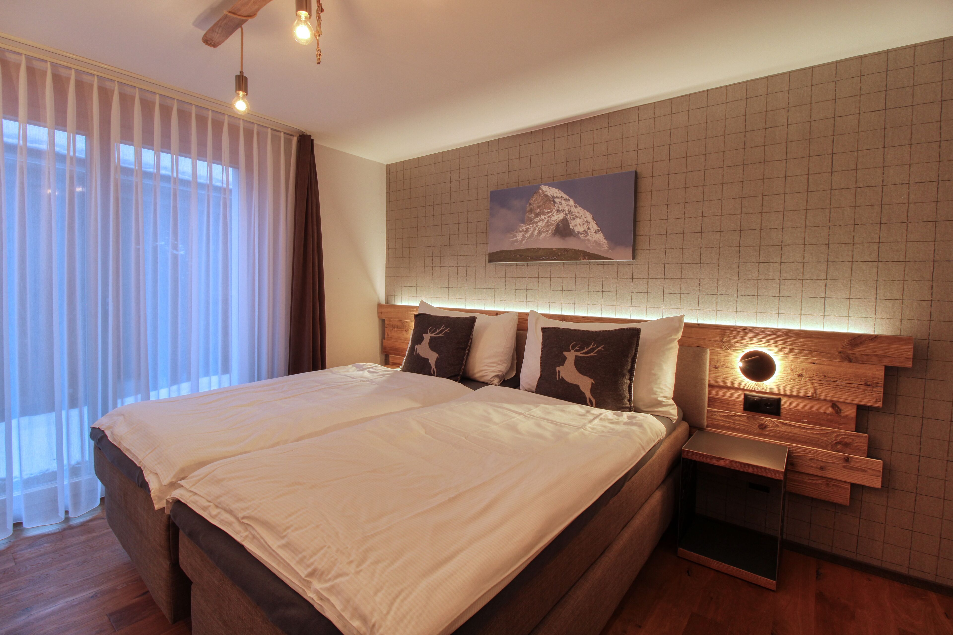 Camera da letto moderna con un letto grande, una testiera in legno e un quadro appeso raffigurante una montagna.