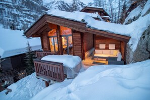 Une cabane en bois dotée d’un balcon, entourée de montagnes enneigées.
