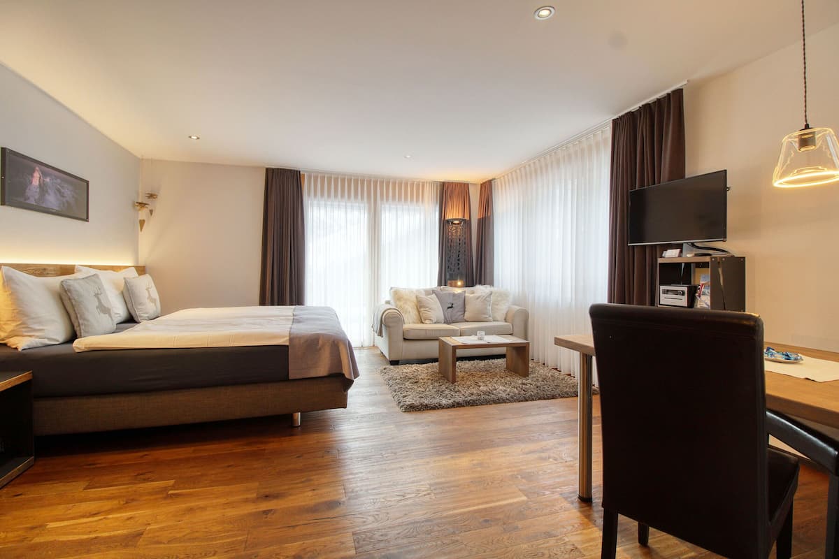 A modern hotel room with a bed, a sofa, a desk, and a TV.