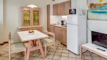 Eine kompakte Küche mit Holzschränken, einem weißen Kühlschrank, einer Mikrowelle und einem Esstisch mit Stühlen.