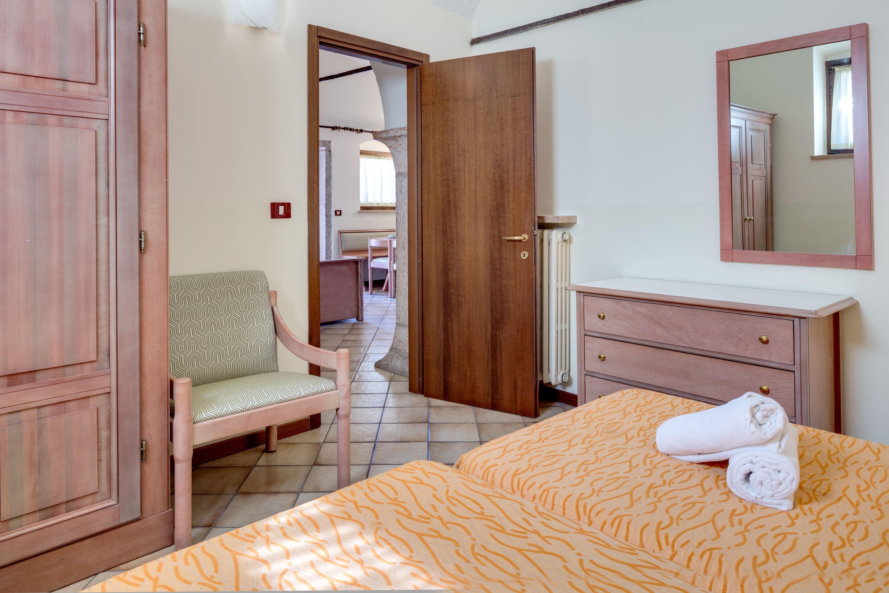 A bedroom with a bed, a chair, a dresser, and a door leading to another room.
