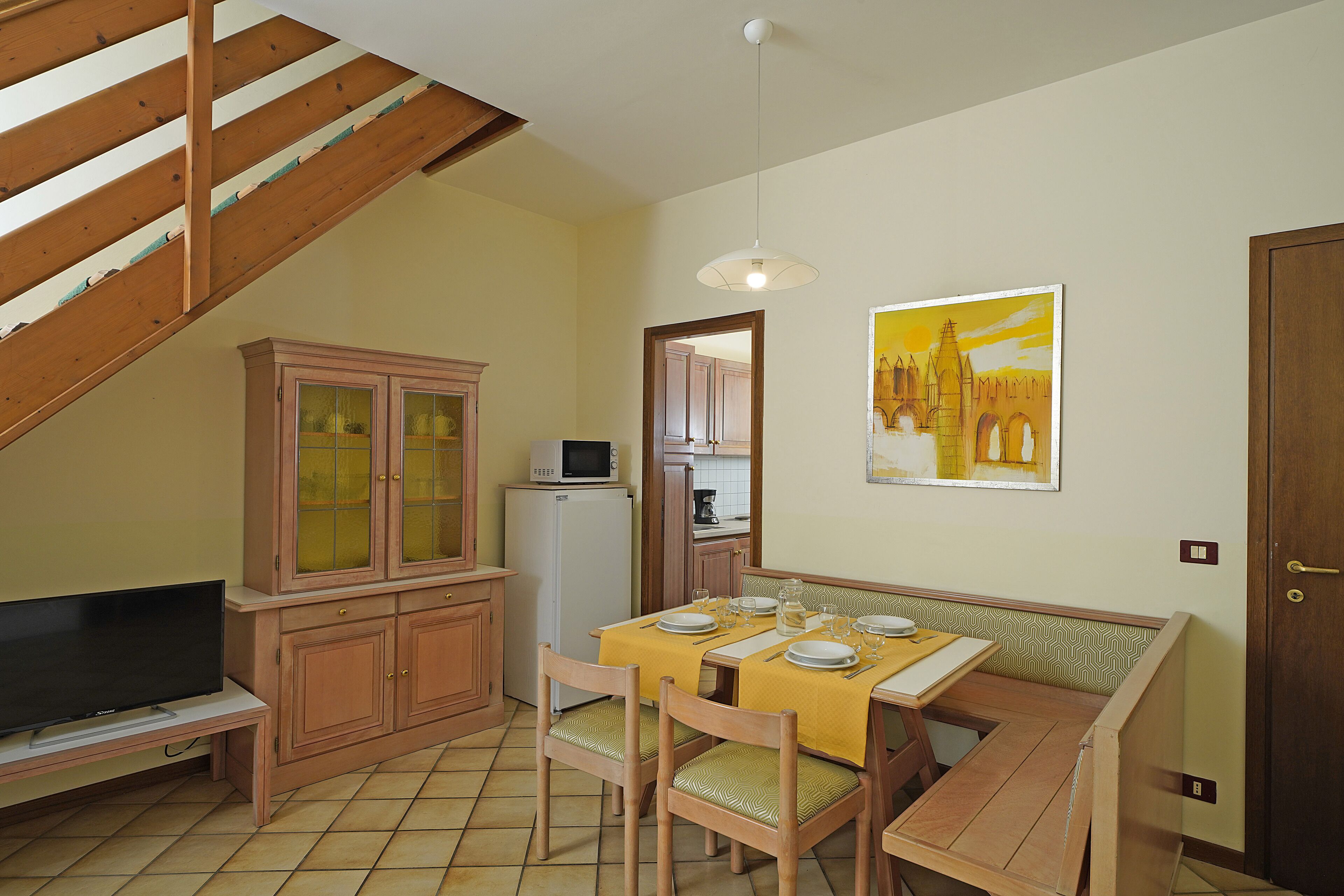 A compact kitchen with wooden cabinets, a microwave, and a dining area with a table set for four.
