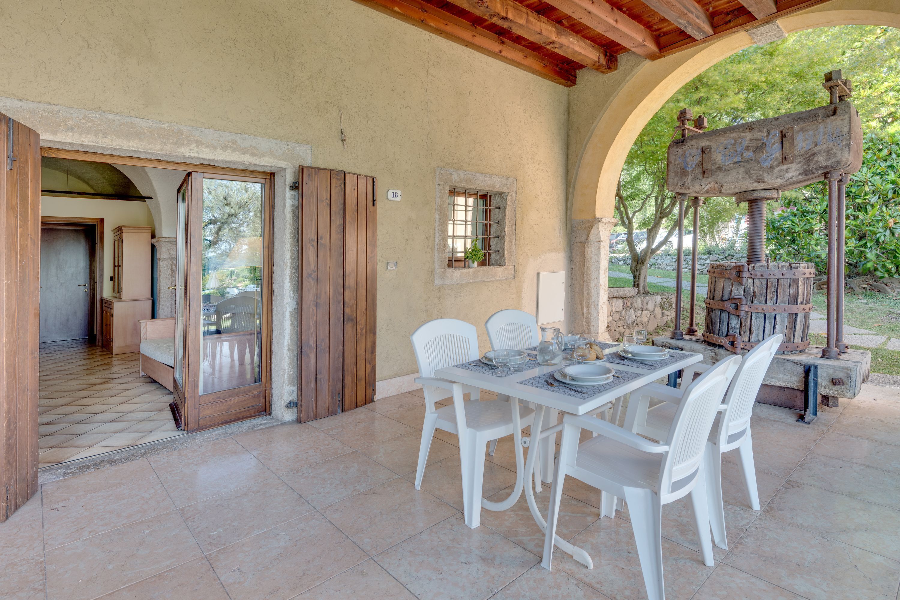 A dining area with a table set for four, white chairs, and a rustic water pump in the background.