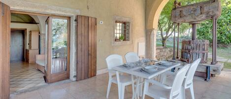 A dining area with a table set for four, white chairs, and a rustic water pump in the background.