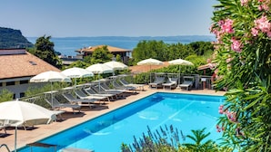A swimming pool with lounge chairs and umbrellas, surrounded by greenery and overlooking a body of water. - Residence La Filanda (Costermano sul Garda)