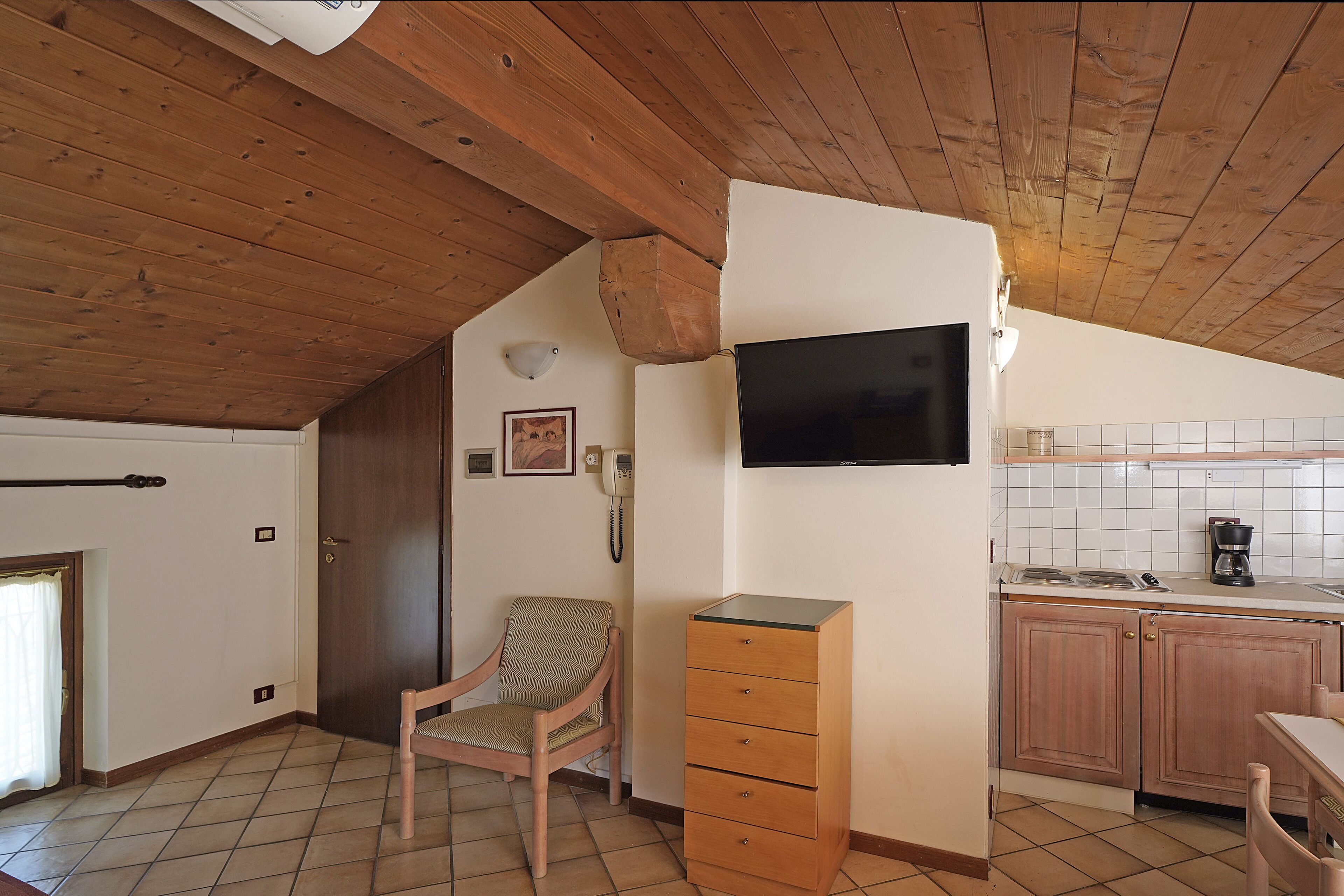 A kitchen with wooden cabinets, a built-in TV, a chair, and a small table.
