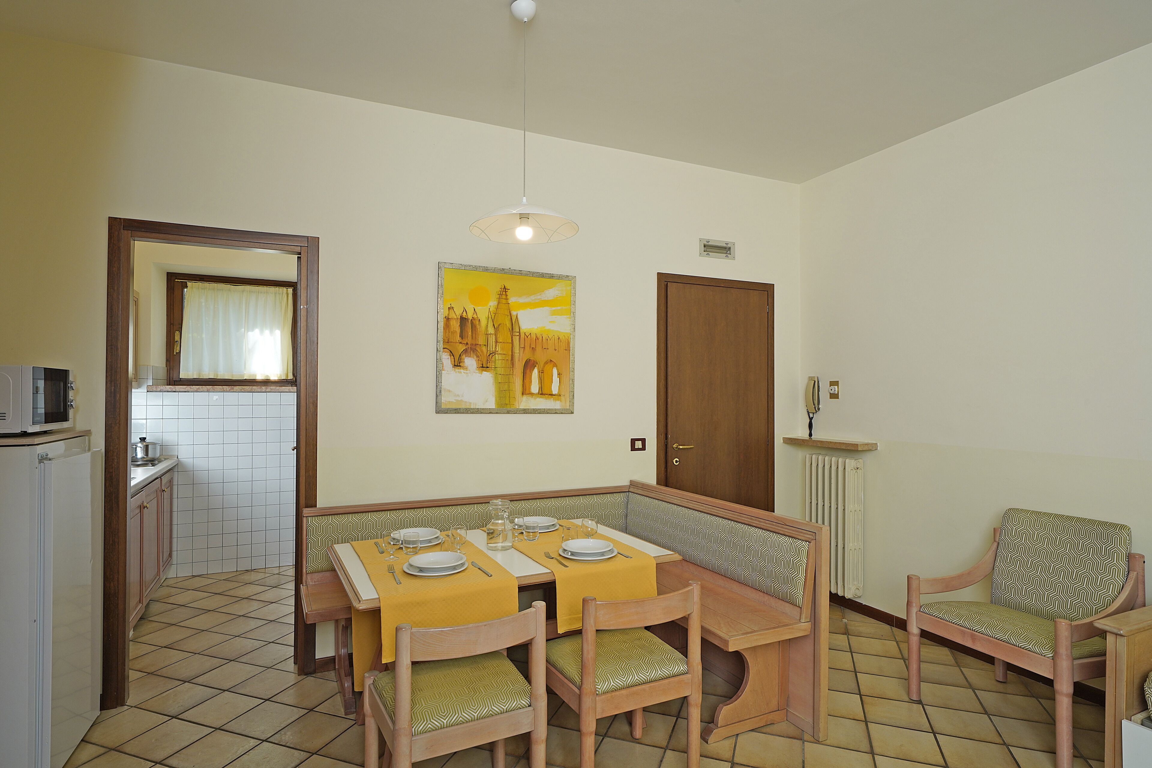 A dining area with a table set for four, a bench, and a chair. A microwave is visible in the corner.