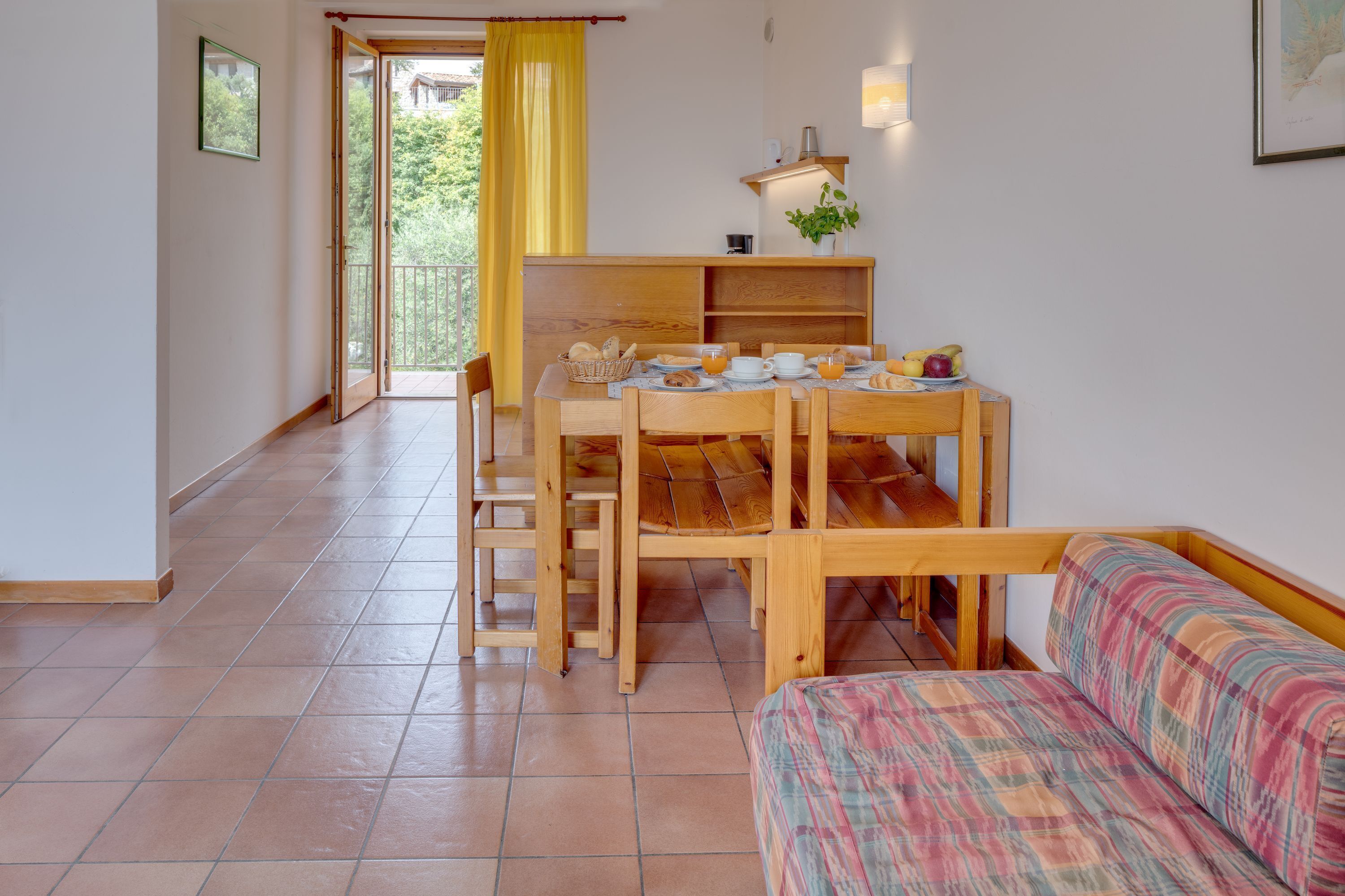 A dining area with a wooden table set for breakfast, a sofa, and a view of the outdoors.
