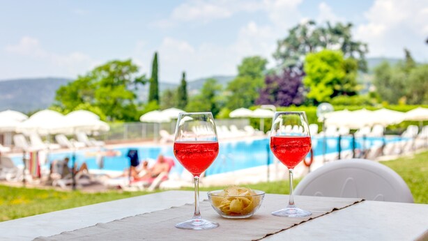 Dos vasos de bebida roja sobre una mesa, con una piscina al fondo.
