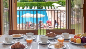 Una mesa de desayuno con cruasanes, fruta y zumo de naranja, con vistas a una piscina y un jardín.