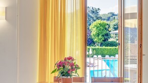 Una mesa de comedor con sillas, una planta en maceta y vista a una piscina a través de un ventanal abierto.